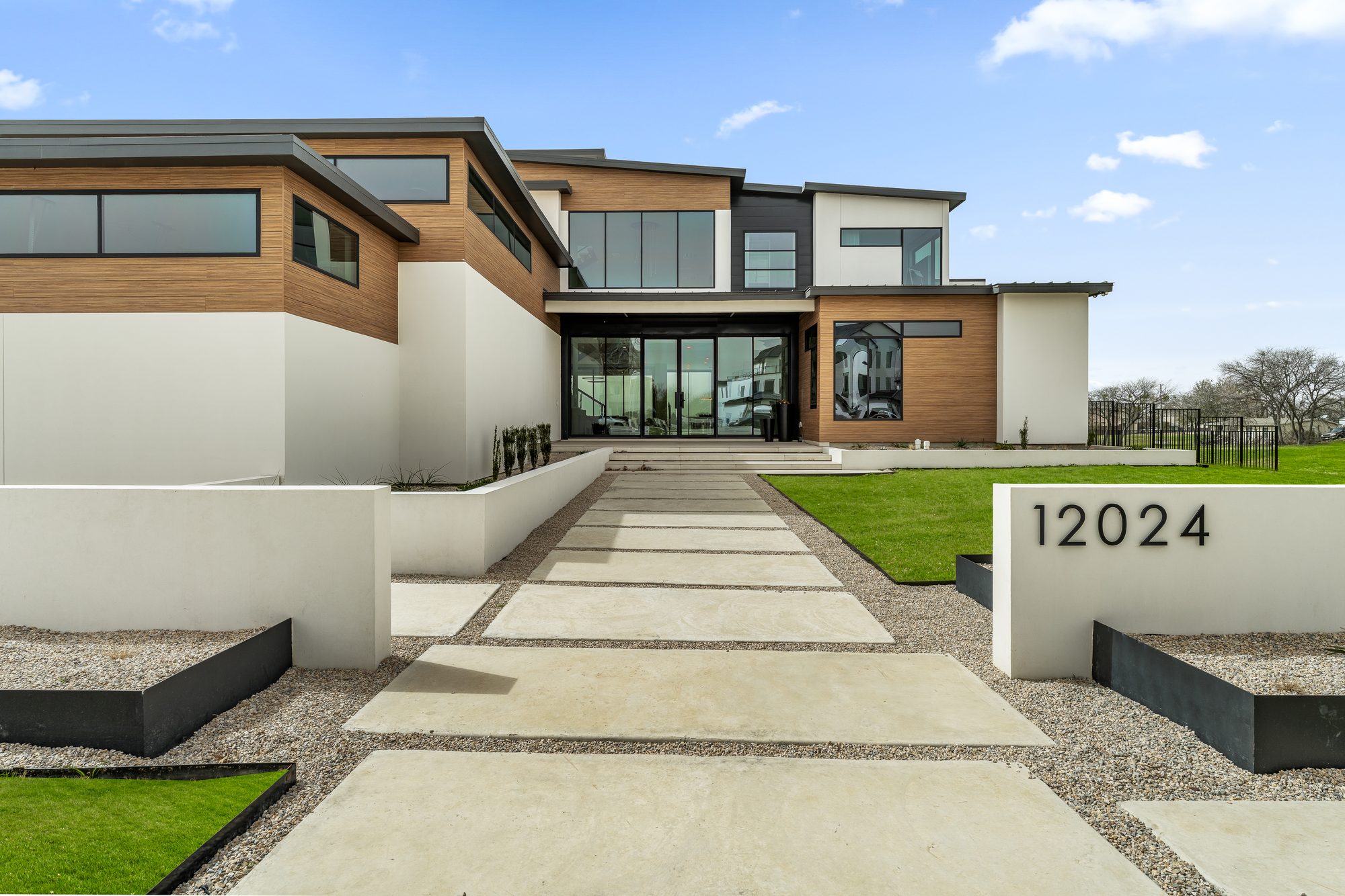 Front of 12024 Blake Place: white stucco, warm horizontal wood, black-framed glass, the address monument, and a modern paver walk