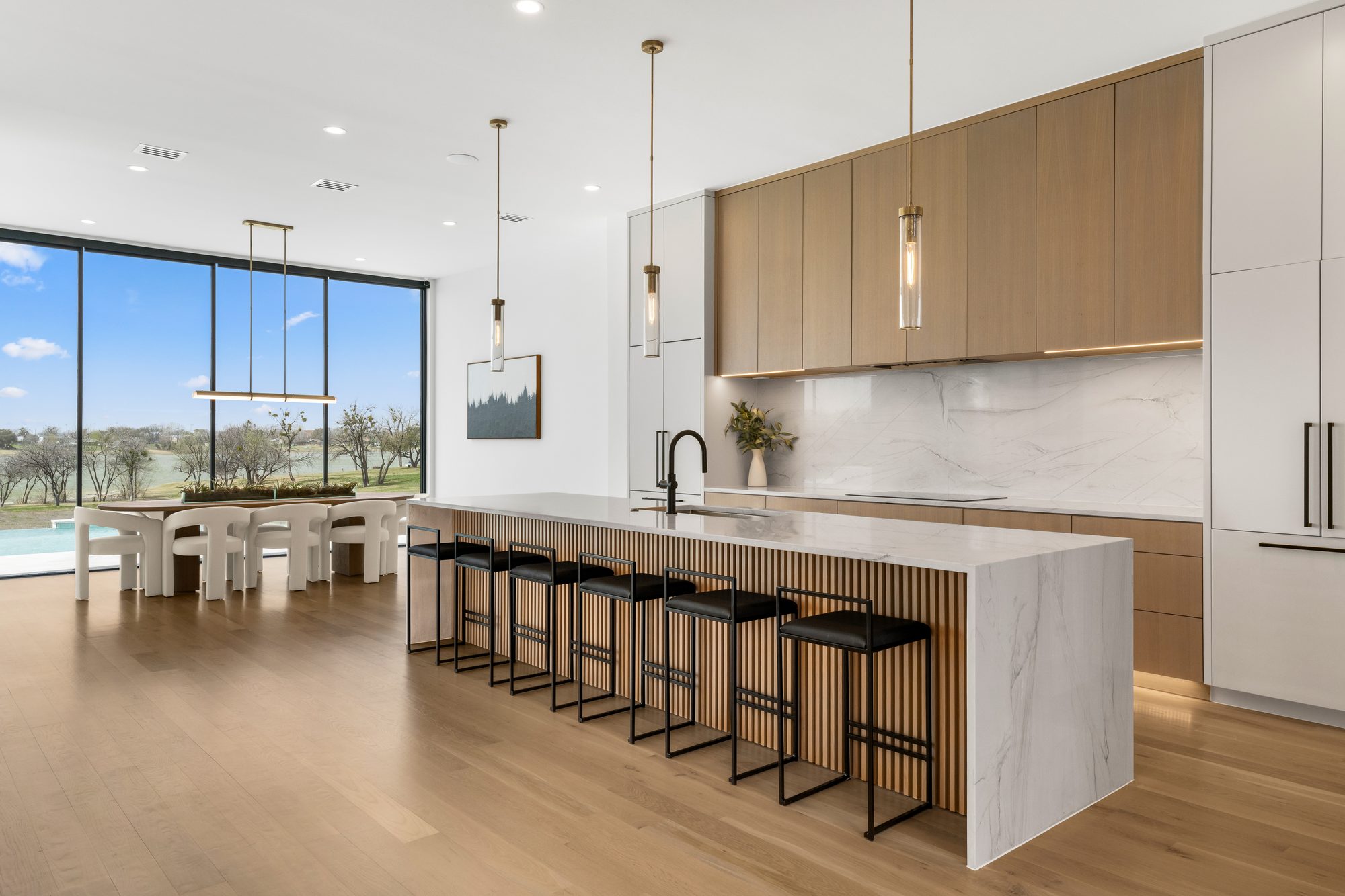 Kitchen waterfall island with a fluted wood base and seating, dining and the lake beyond