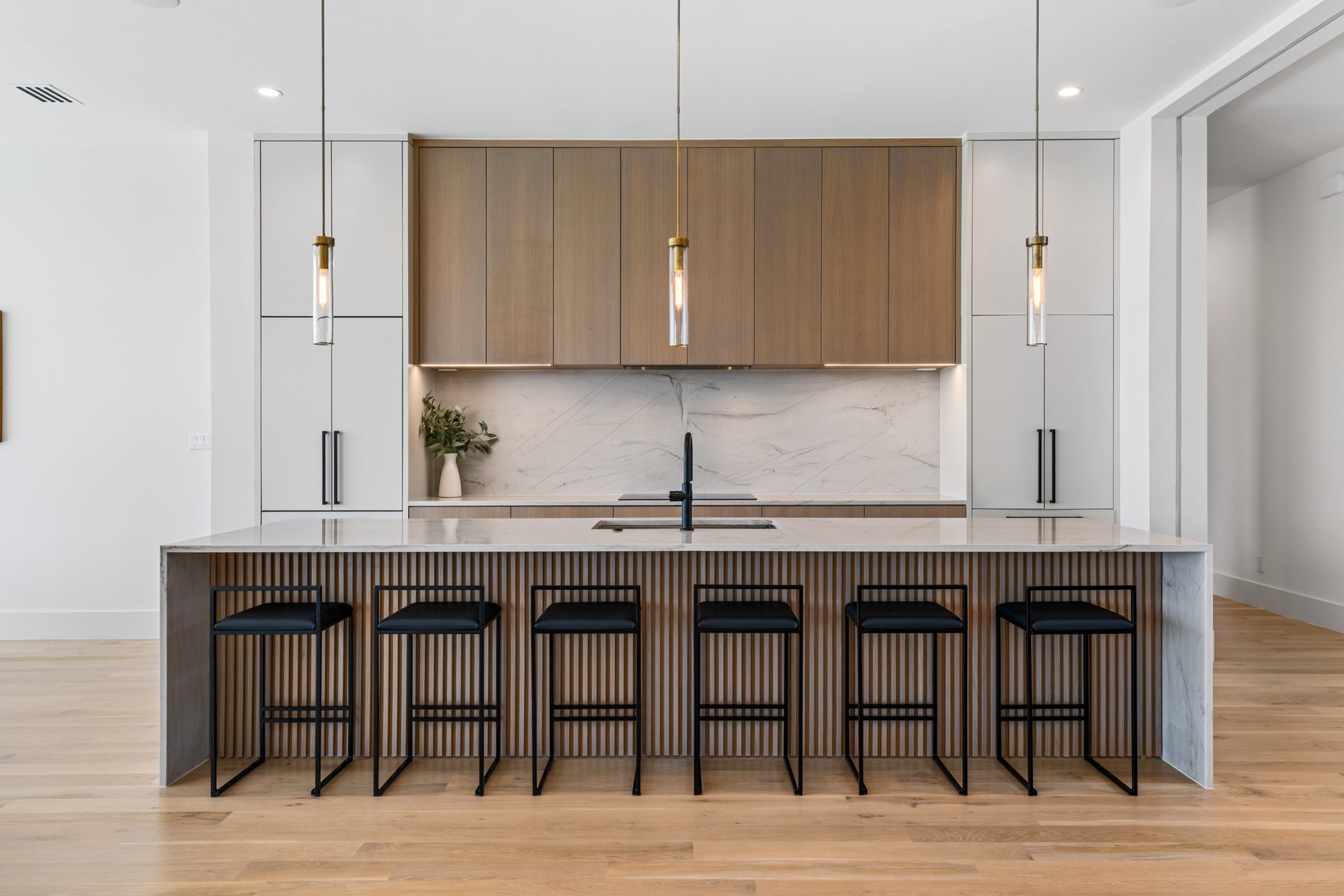 Kitchen island head-on, with warm wood cabinetry, a marble backsplash, and pendant lighting